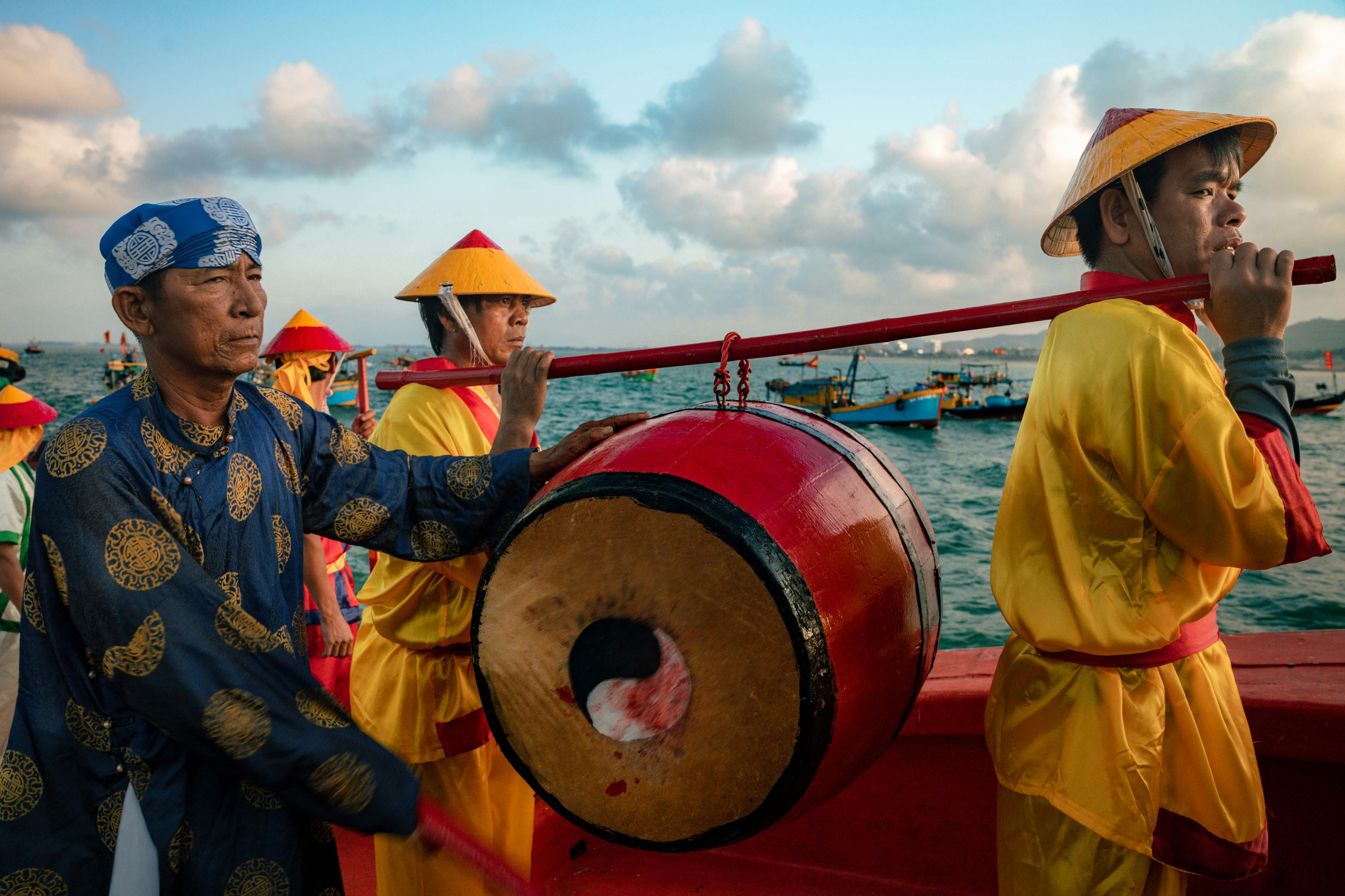 Ceremonial procession with drum on a boat in Vietnam's vibrant sea backdrop.