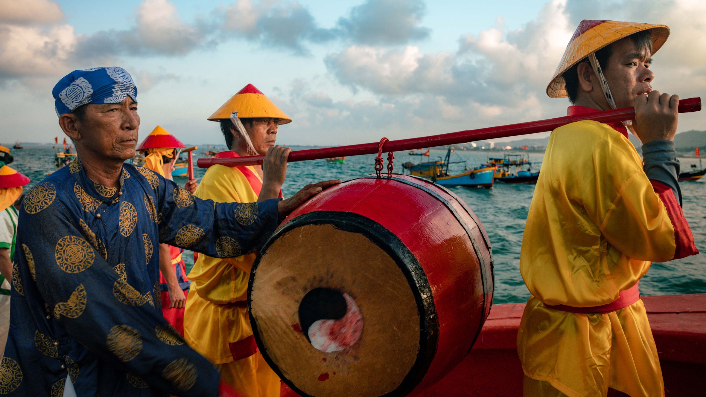 Ceremonial procession with drum on a boat in Vietnam's vibrant sea backdrop.