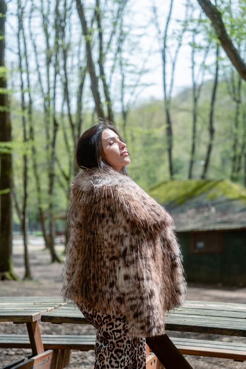 Free A woman in a fur coat stands outdoors in a serene forest setting, enjoying nature. Stock Photo