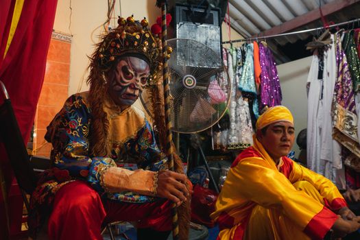 Two Chinese opera performers in ornate costumes preparing backstage before a performance.