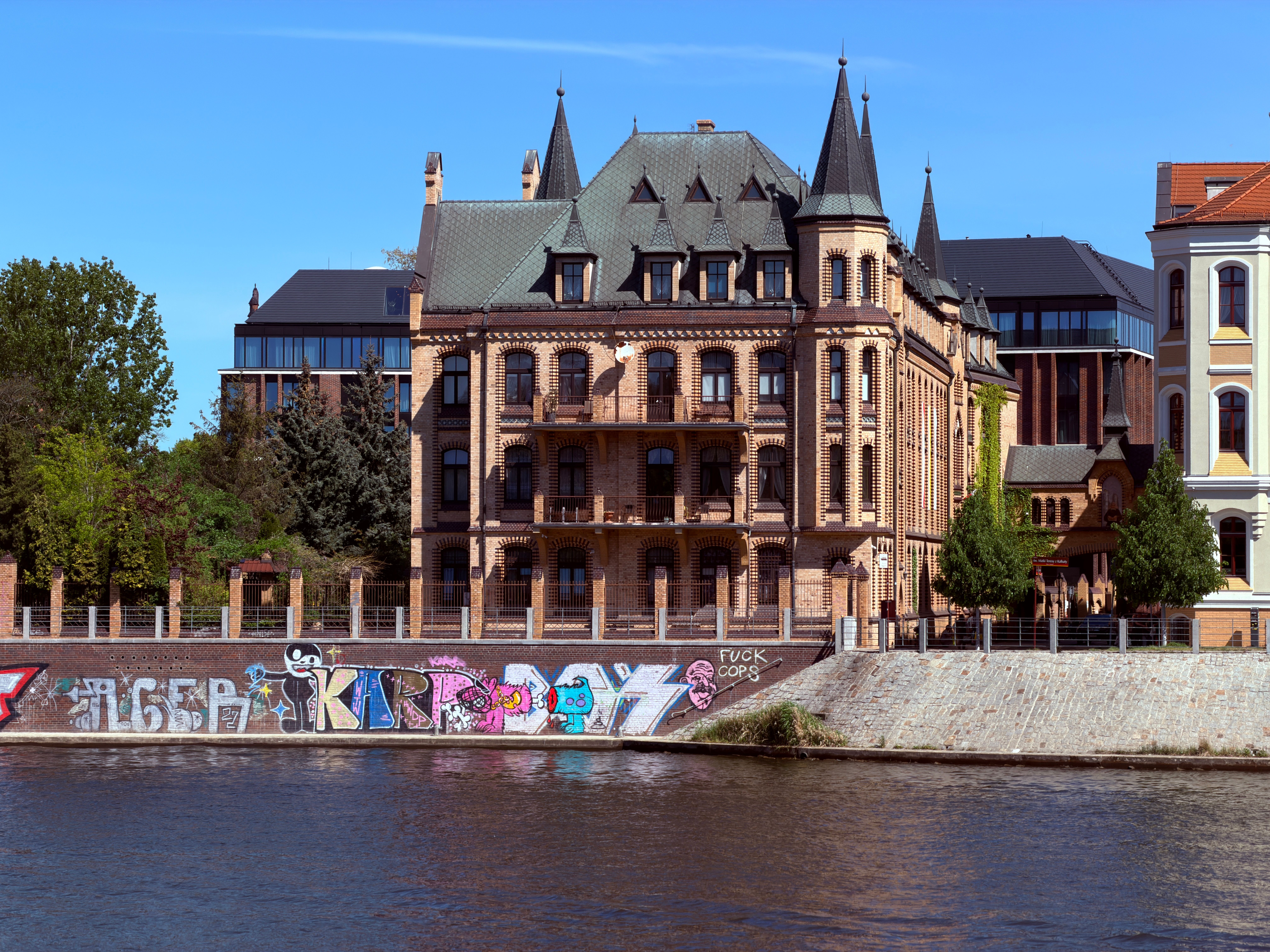 A historic building in Wrocław, Poland with colorful graffiti, viewed from across the river.