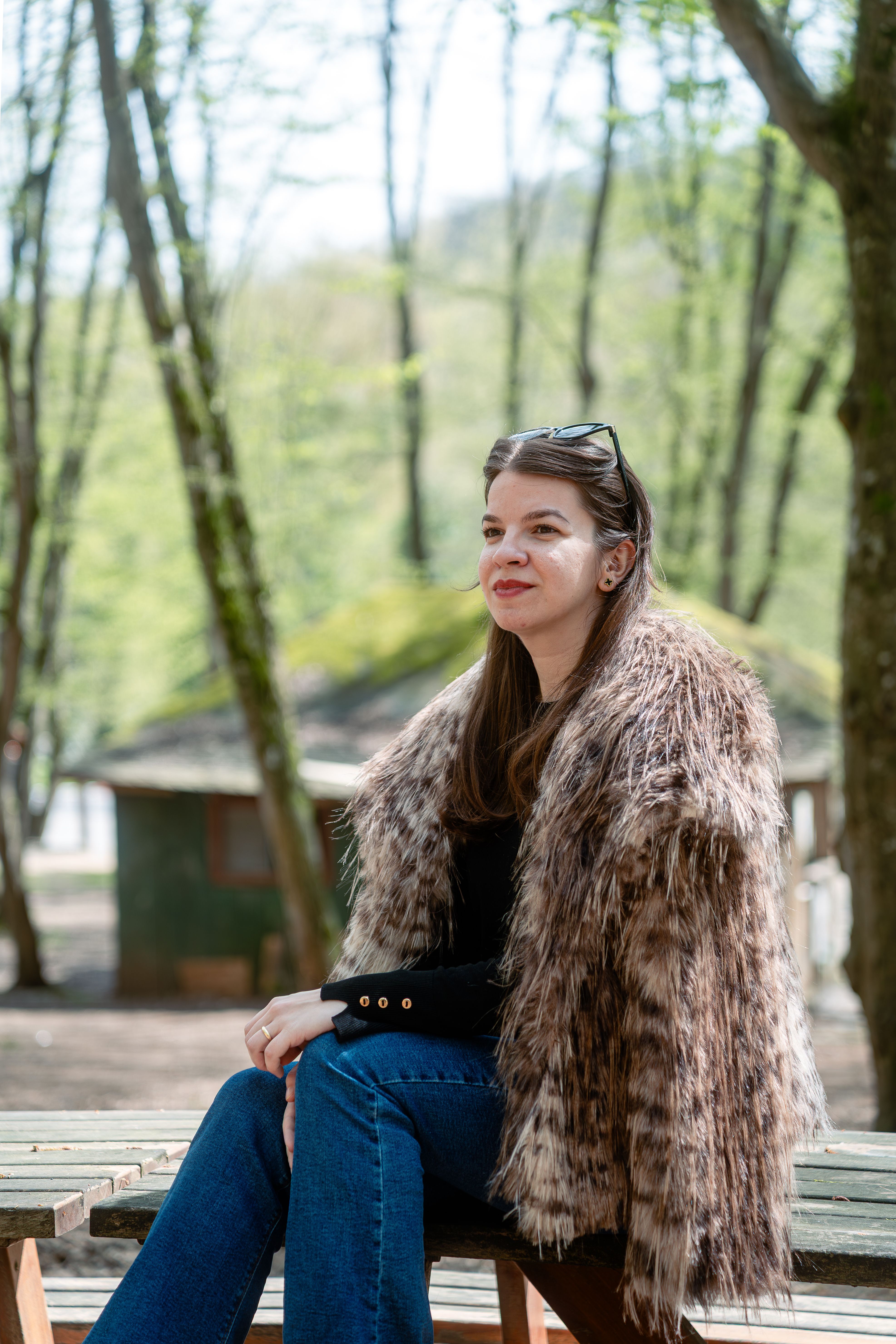 Woman in faux fur coat sitting at park bench enjoying the springtime scenery.