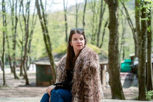 Free A woman in a fur coat sits outdoors in a spring forest. Sunny day setting. Stock Photo