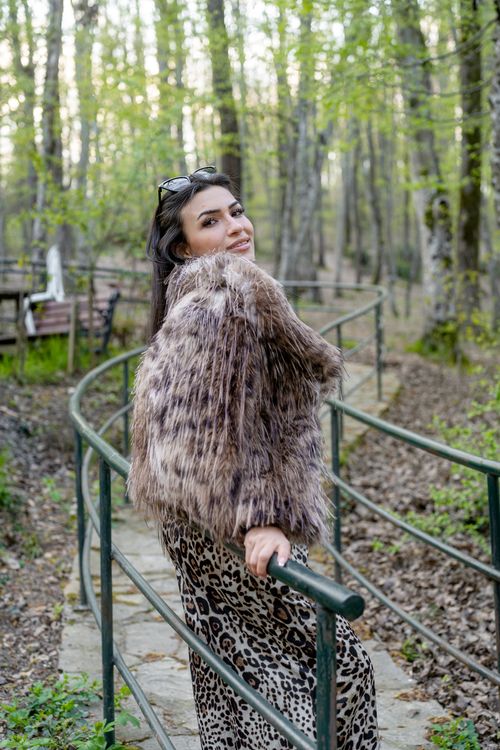 Free Fashionably dressed woman in fur coat smiles while strolling through a lush spring forest. Stock Photo