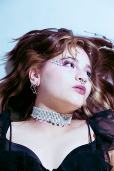 Stylish young woman with rhinestone jewels and goth accessories posing indoors.