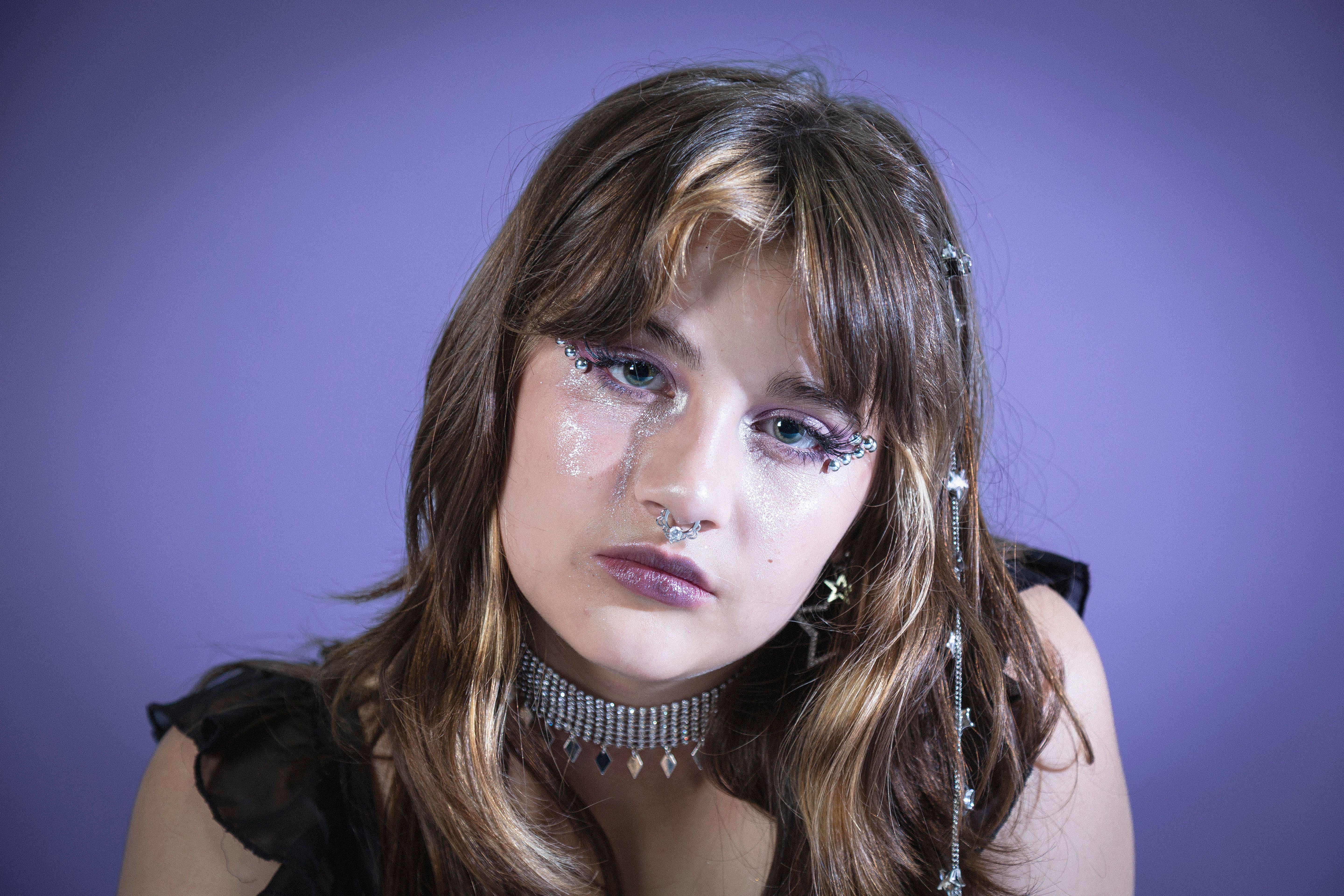 Fashion portrait showcasing glam makeup and accessories against a purple background.
