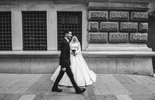 A bride in a wedding dress and groom in motion in black and white against a textured urban backdrop.