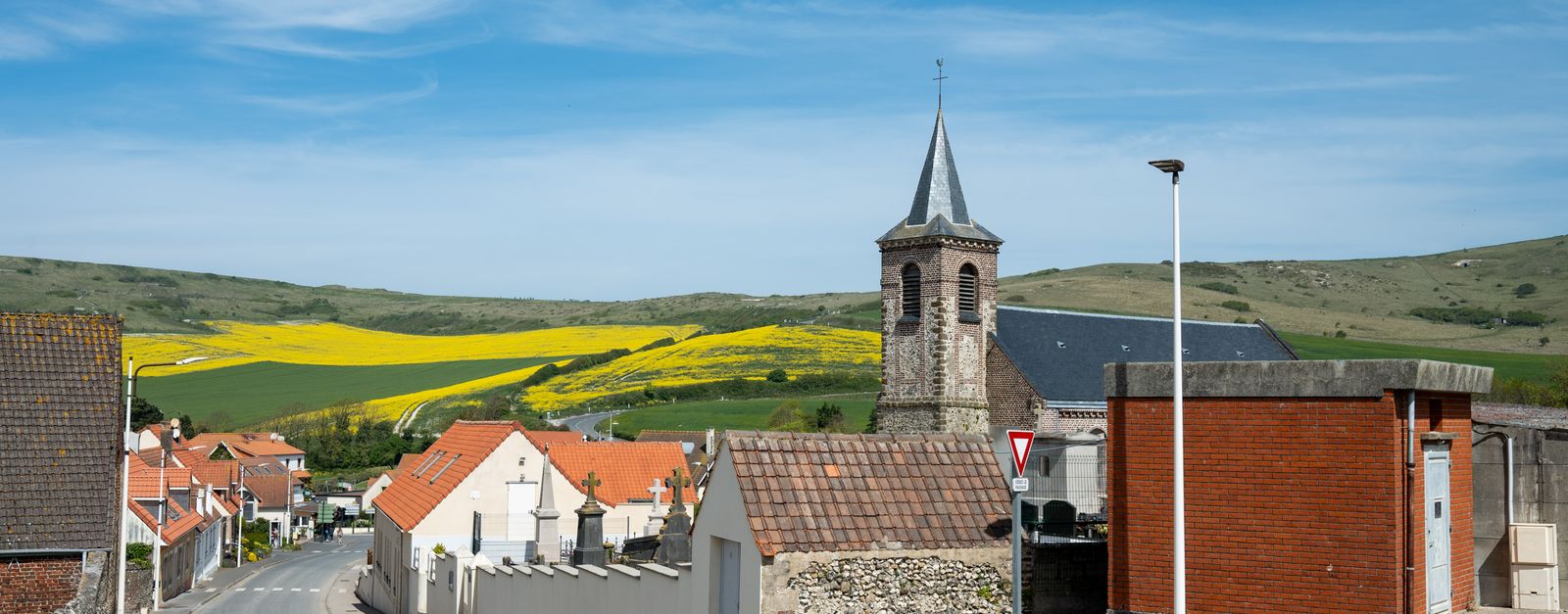Charming village scene in Escalles, France with church tower and vibrant yellow fields.
