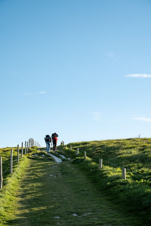 Free Two hikers on a grassy path in Escalles, France under a clear blue sky. Stock Photo