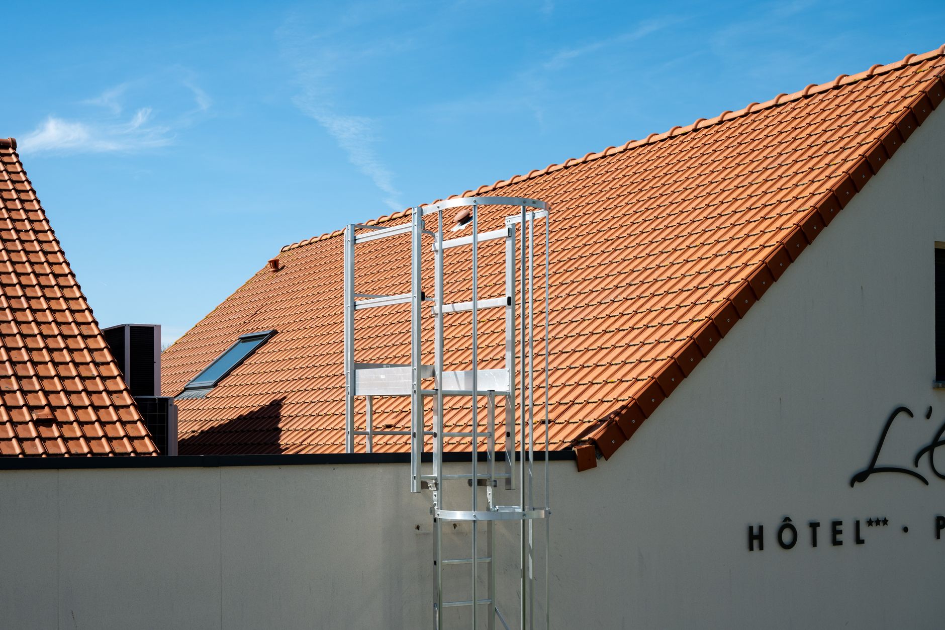 Sunny view of a hotel rooftop with ladder, featuring terracotta tiles and blue sky in Escalles, France.