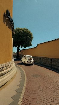 Classic small car on a narrow, charming European street during the day.