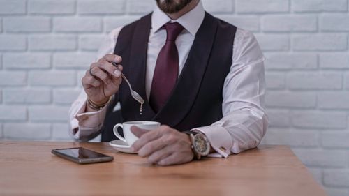Free Businessman in formal attire stirring coffee at a desk, indoors. Stock Photo