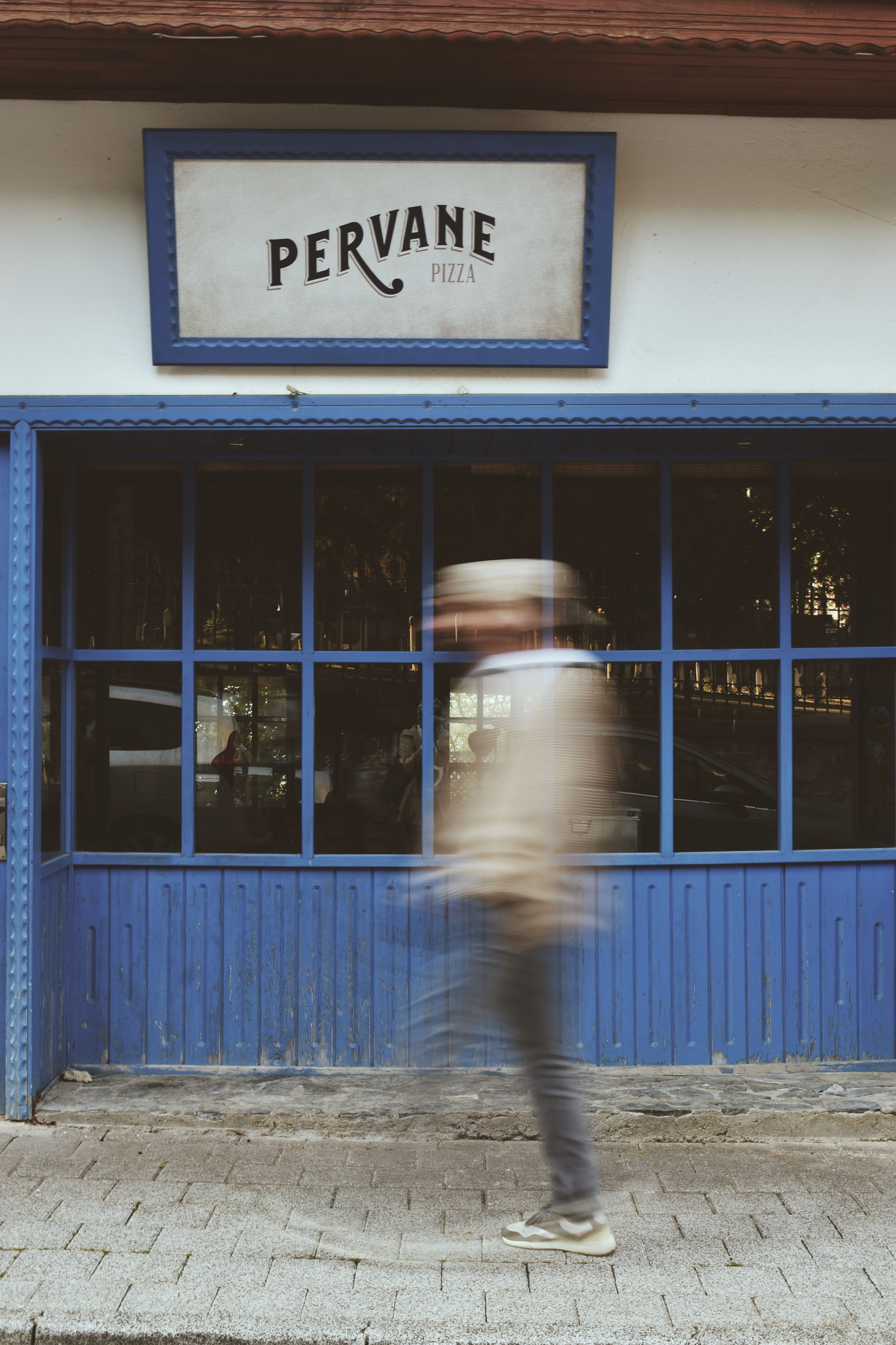 A person walks briskly past the Pervane Pizza shop, creating a blurred motion effect against the blue facade.