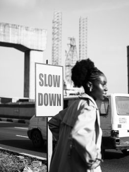 Black and white photo of a street scene in Lagos, Nigeria, featuring a 'Slow Down' sign and a blurred pedestrian.