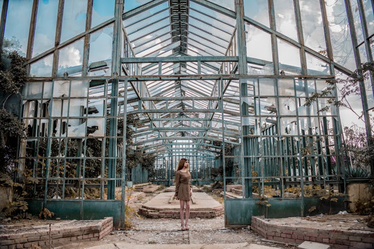 Unrecognizable Woman Standing Near Old Metal Construction Under Cloudy Sky