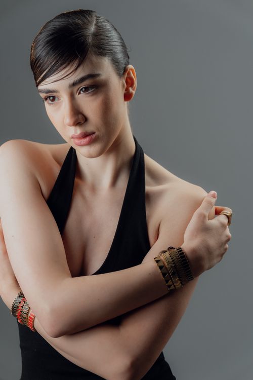 Free A contemplative woman in a black dress with stylish bracelets, set against a neutral background. Stock Photo