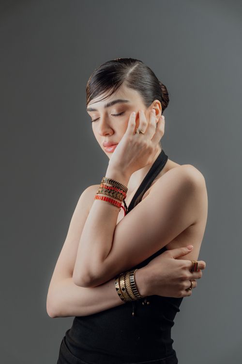 Free Portrait of a stylish woman wearing bracelets, lost in thought with a serene expression against a gray backdrop. Stock Photo