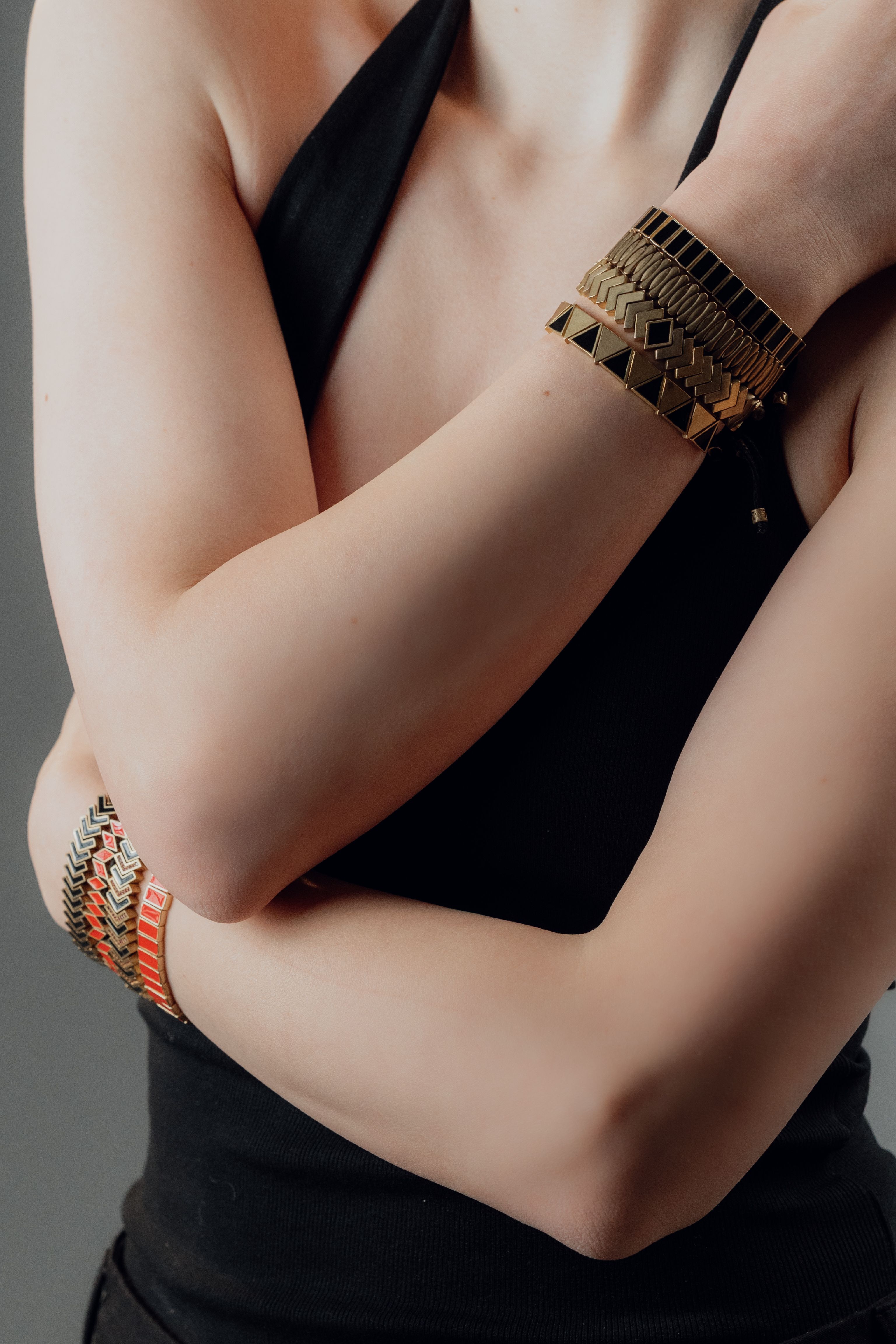 Close-up dos braços de uma mulher adornados com pulseiras estilosas, exibindo moda moderna em um fundo neutro.