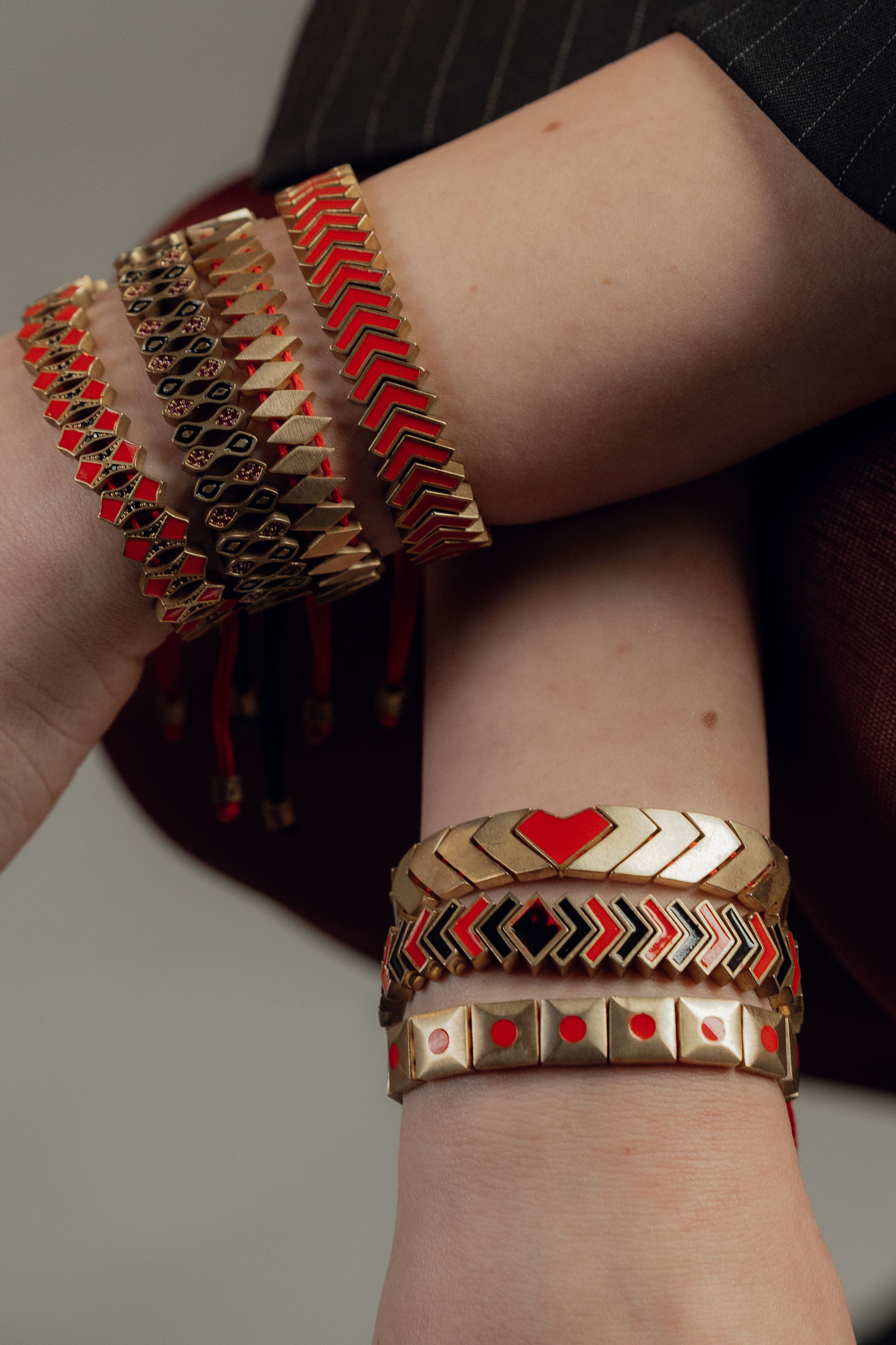 Elegante coleção de pulseiras douradas e vermelhas com padrões, usadas em braços cruzados, exibindo um estilo de joalheria sofisticado.