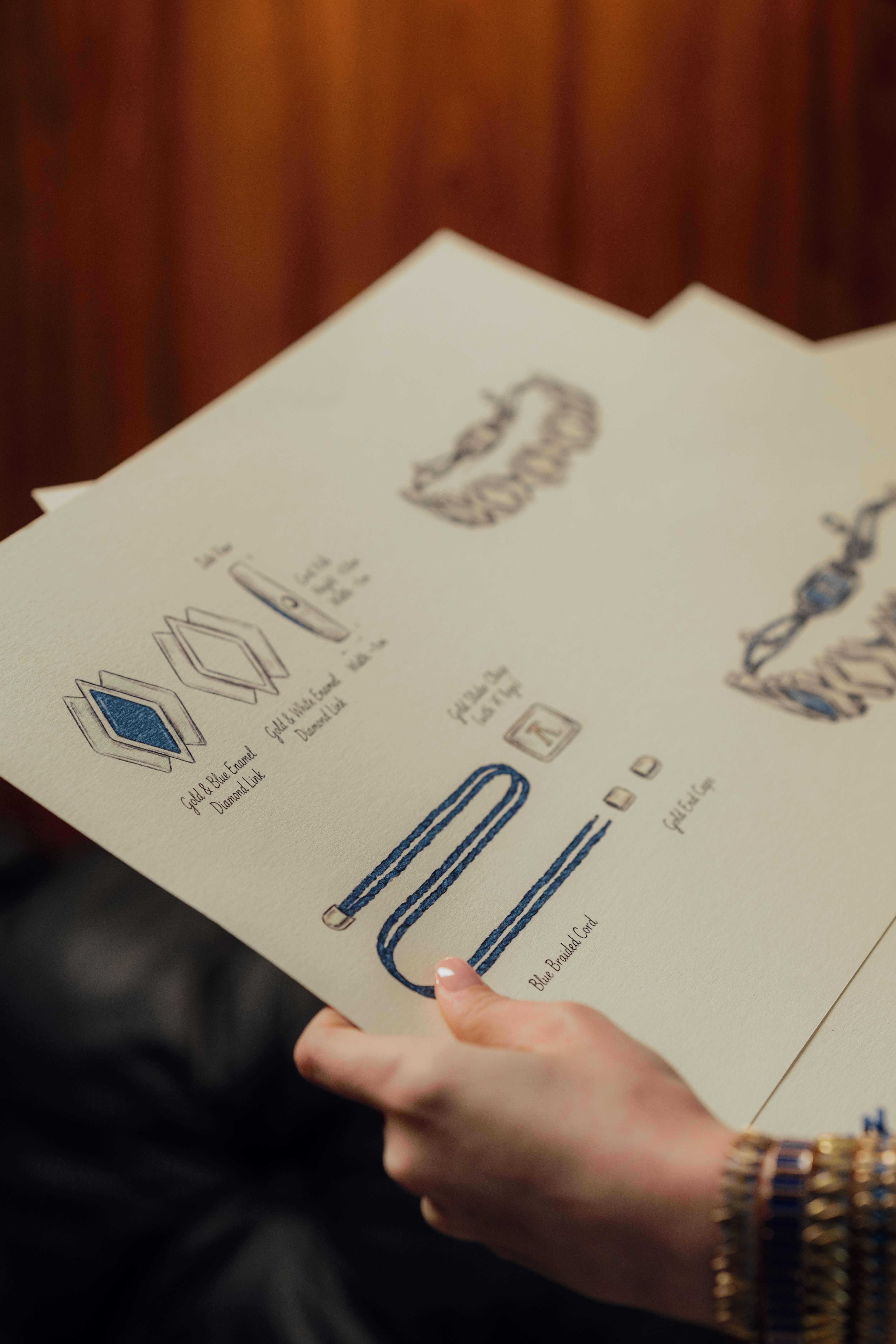 Close-up of a person holding jewelry design sketches with blueprints and diagrams.