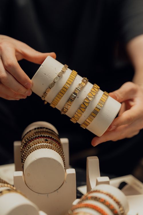 Free Detailed close-up of hands arranging gold bracelets on a white display stand indoors. Stock Photo