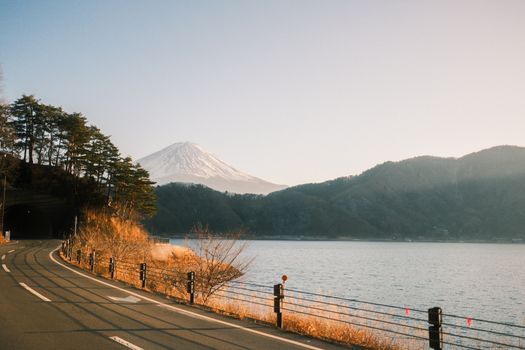 Serene lakeside road with Mount Fuji backdrop in Fujikawaguchiko, Japan during sunset.