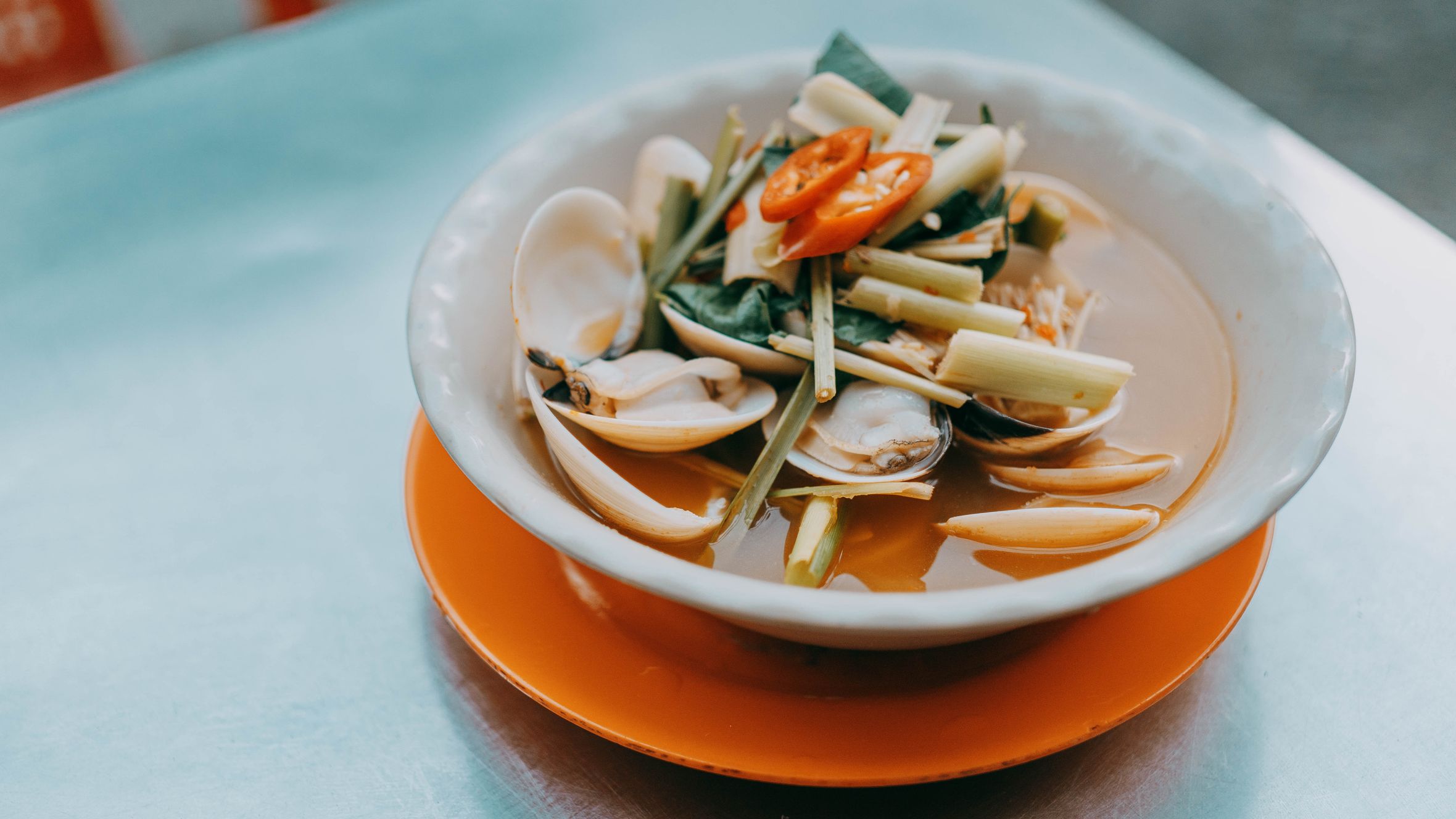 A flavorful Asian clam soup garnished with lemongrass and sliced red peppers, served in an elegant bowl.