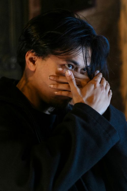 Free A thoughtful young man covering his face with his hands, captured in moody lighting, indoors. Stock Photo