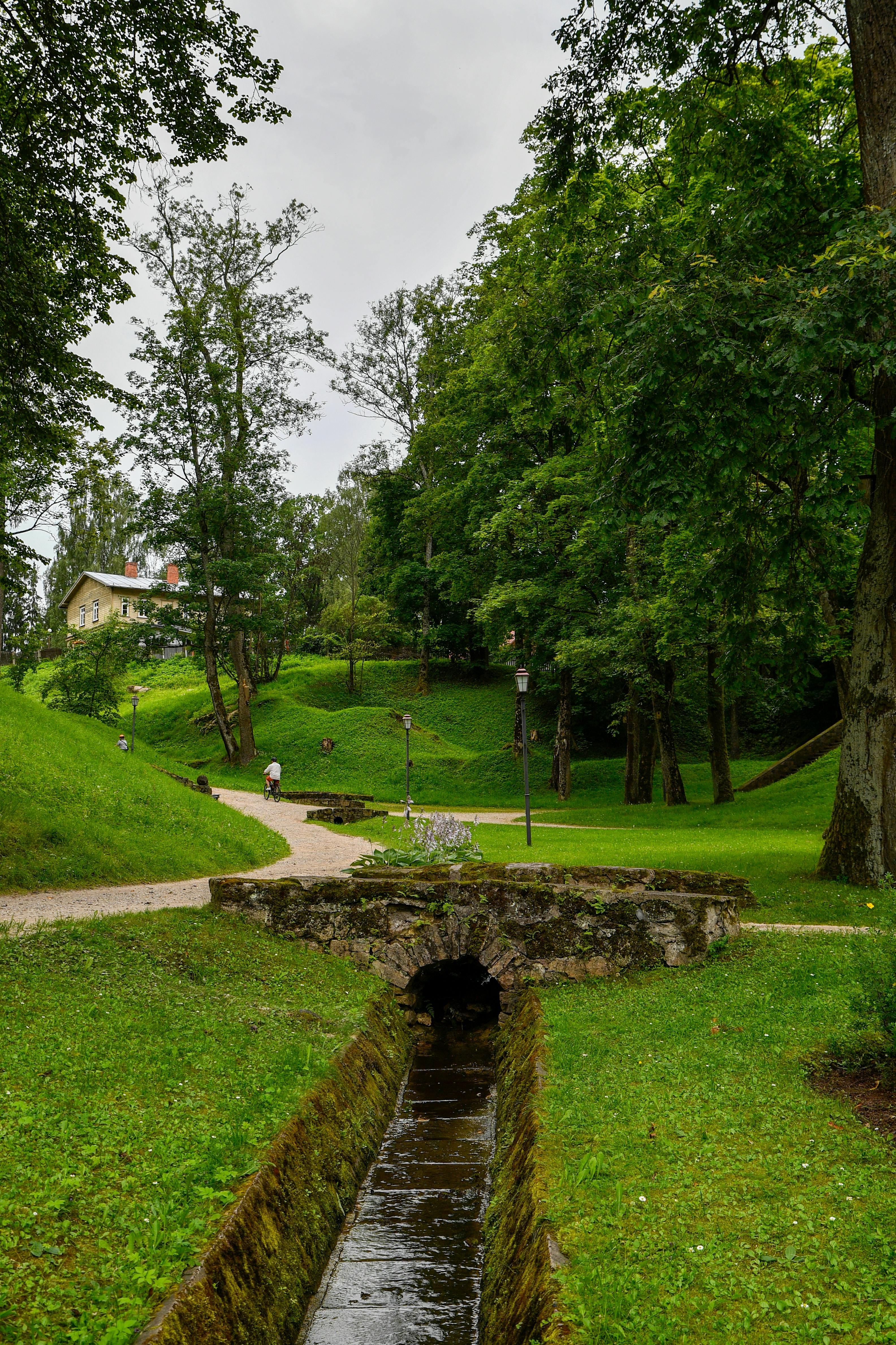 Peaceful summer scene of a historic stone bridge over a stream in Cēsis Park, Latvia.