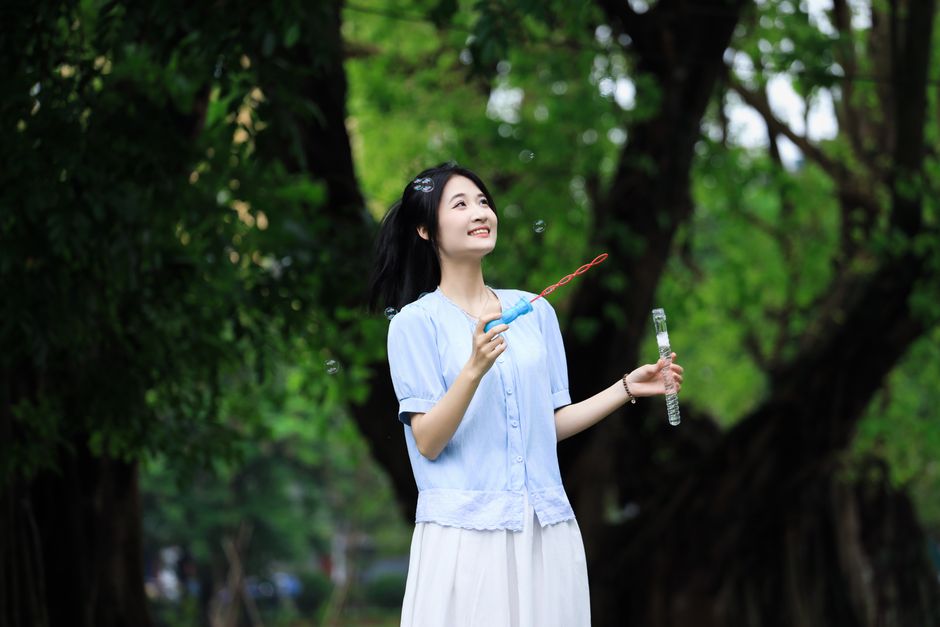 A cheerful young woman enjoys blowing bubbles in a vibrant Vietnamese park.
