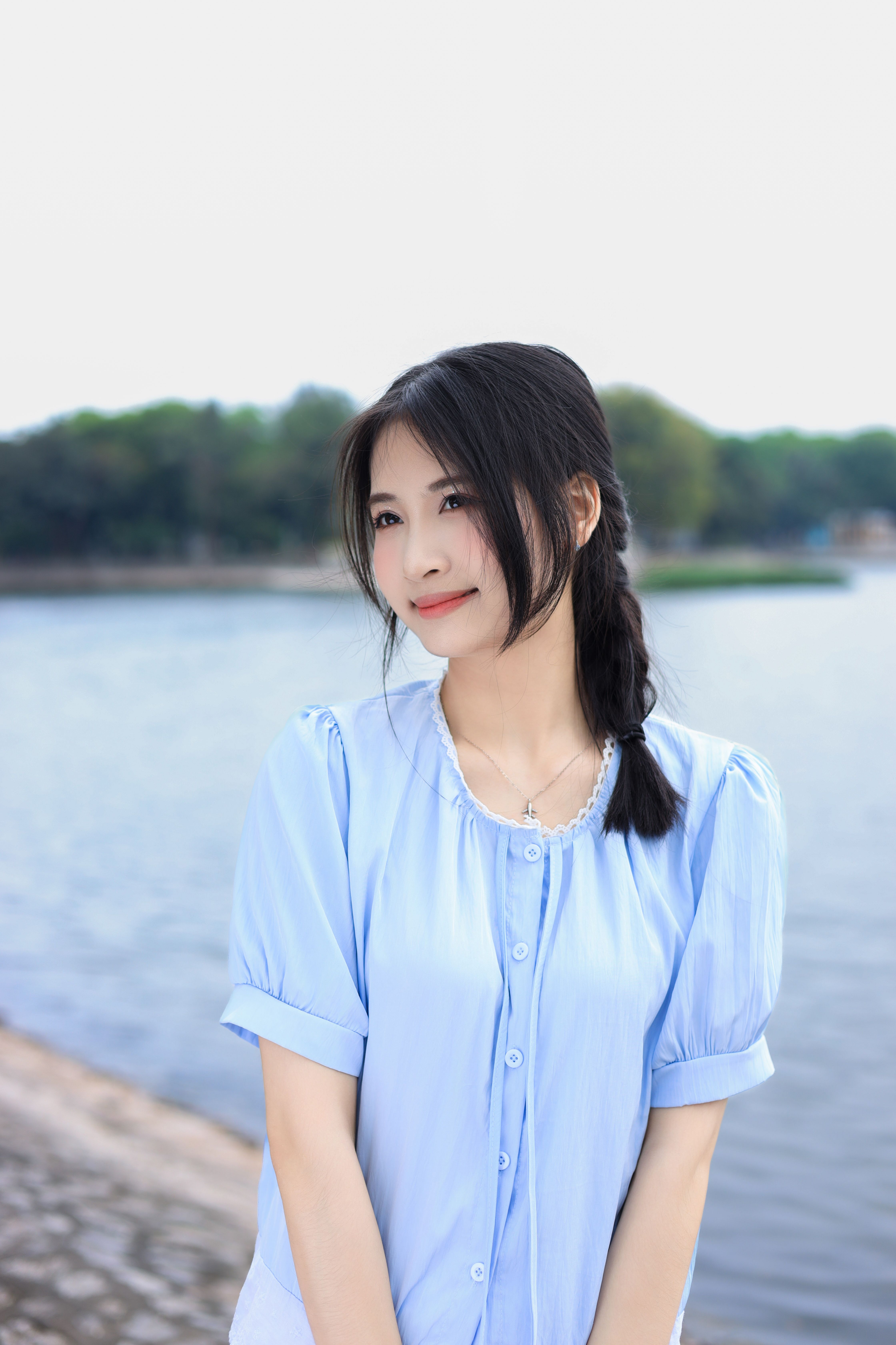 Portrait of a young woman standing by the serene waterside in Hanoi, Vietnam.