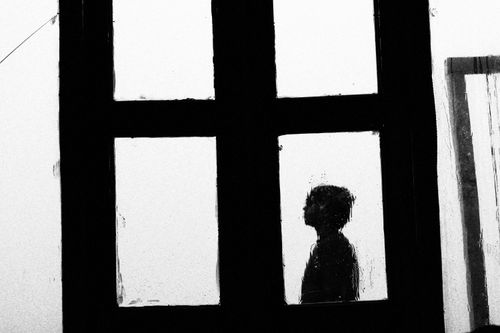 Free Black and white silhouette of a child through a rain-soaked window, evoking solitude. Stock Photo
