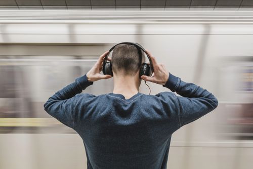 Free A young man wearing headphones stands in a subway station, focusing on music. Stock Photo