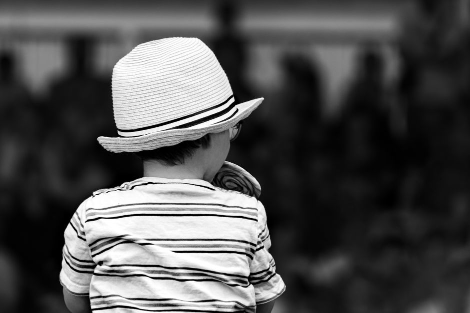 Una foto en blanco y negro que captura a un niño pequeño con camiseta a rayas y sombrero desde atrás, creando una sensación vintage.