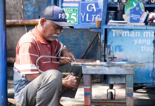 Free Elderly man focuses on cutting a piece of wood with a hand saw in a blue-toned workshop. Stock Photo