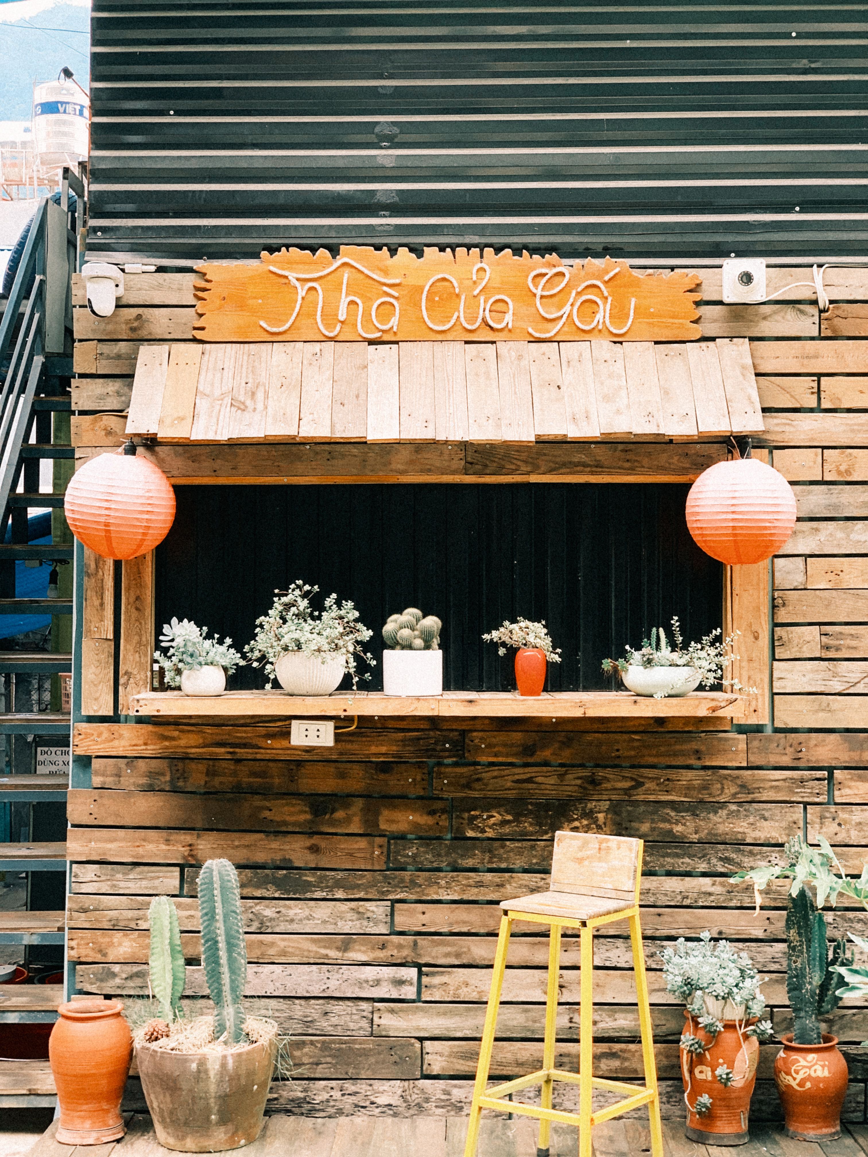 Charming wooden café facade with potted plants, red lanterns, and a yellow chair.