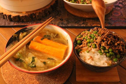 A warm and inviting Asian meal featuring a soup with vegetables and a rice bowl topped with meat and peas.