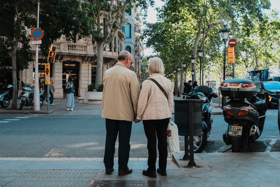 Una pareja de ancianos tomados de la mano en un día soleado en el paisaje urbano de Barcelona.