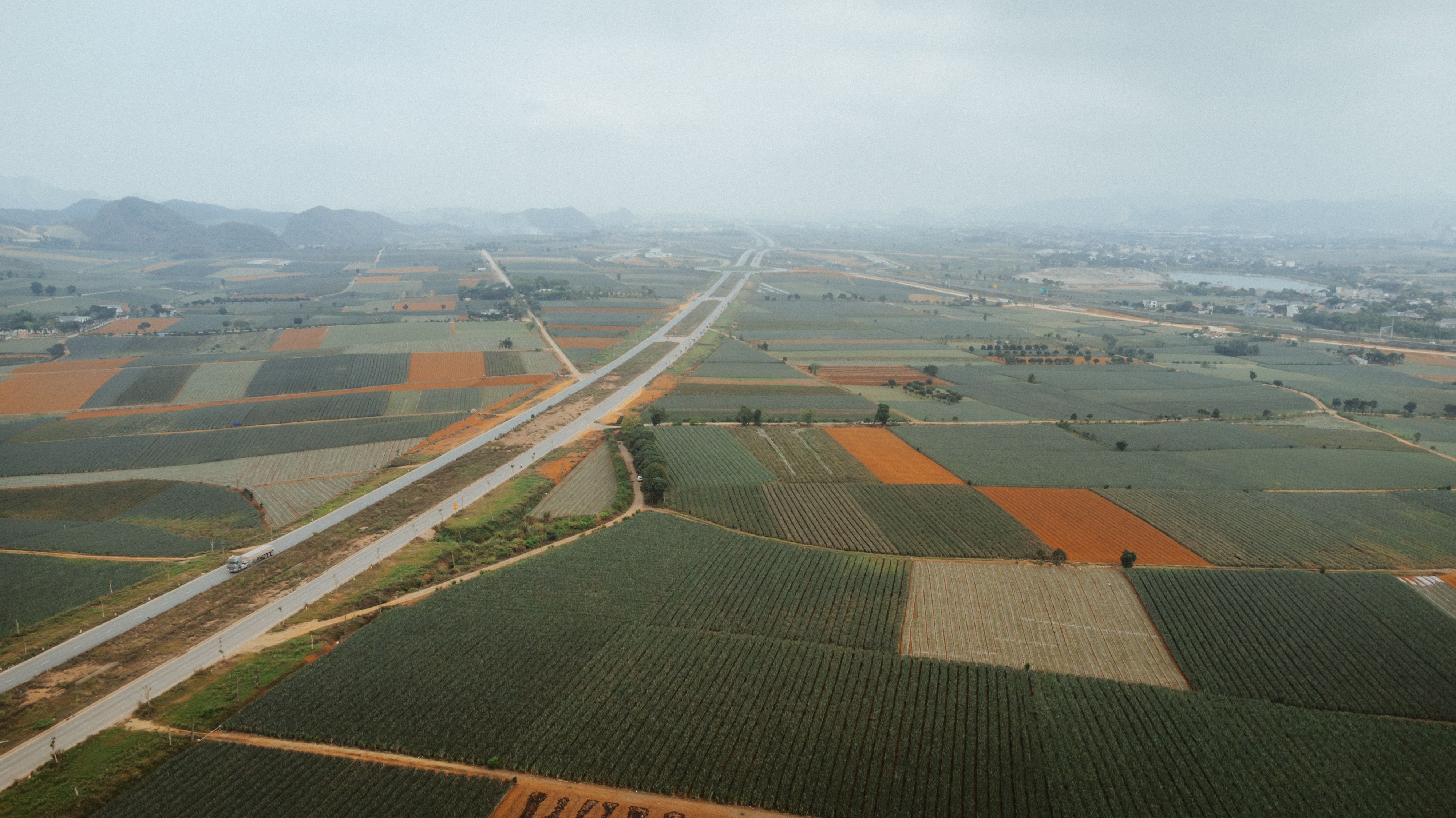 Wide highway approach to Manesar, Gurugram, with industrial plots and green ridges