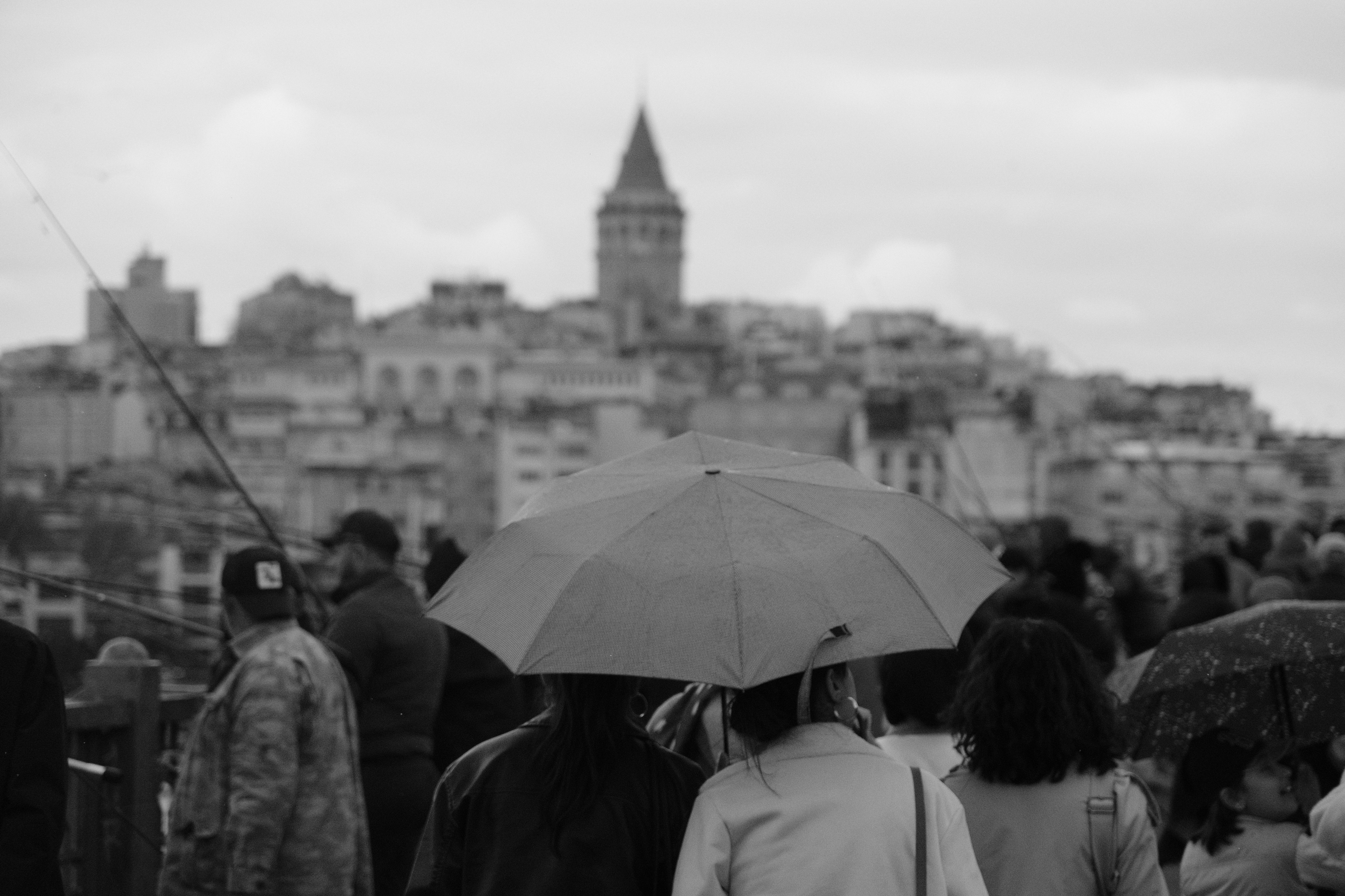 Black and white cityscape of Istanbul with Galata Tower and people under umbrellas.