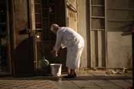 An elder man washes his hands with a towel in a street in Yidda, Saudi Arabia.