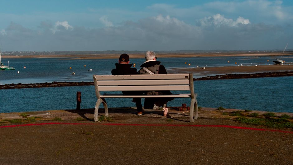 Elderly couple sitting on a bench by the sea, enjoying the view in Le Croisic, France.