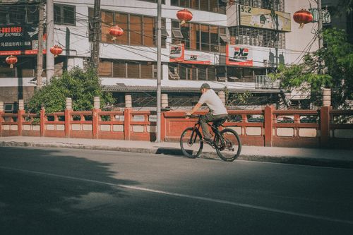 Free A man rides a bicycle past a red bridge in Metro Manila, Philippines, during the day. Stock Photo