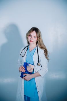 Portrait of a female doctor in scrubs holding a medical book and stethoscope, embodying professionalism and healthcare.