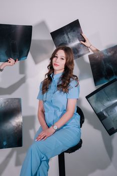 A female doctor in scrubs surrounded by x-ray images in a studio setting.