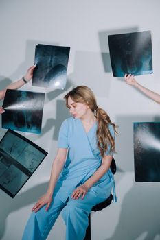Female doctor in blue scrubs examines X-rays in a clinical setting with multiple hands holding films.