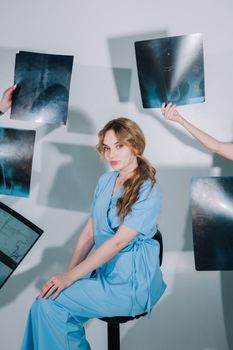 A female healthcare worker in blue scrubs reviews multiple X-ray images indoors.