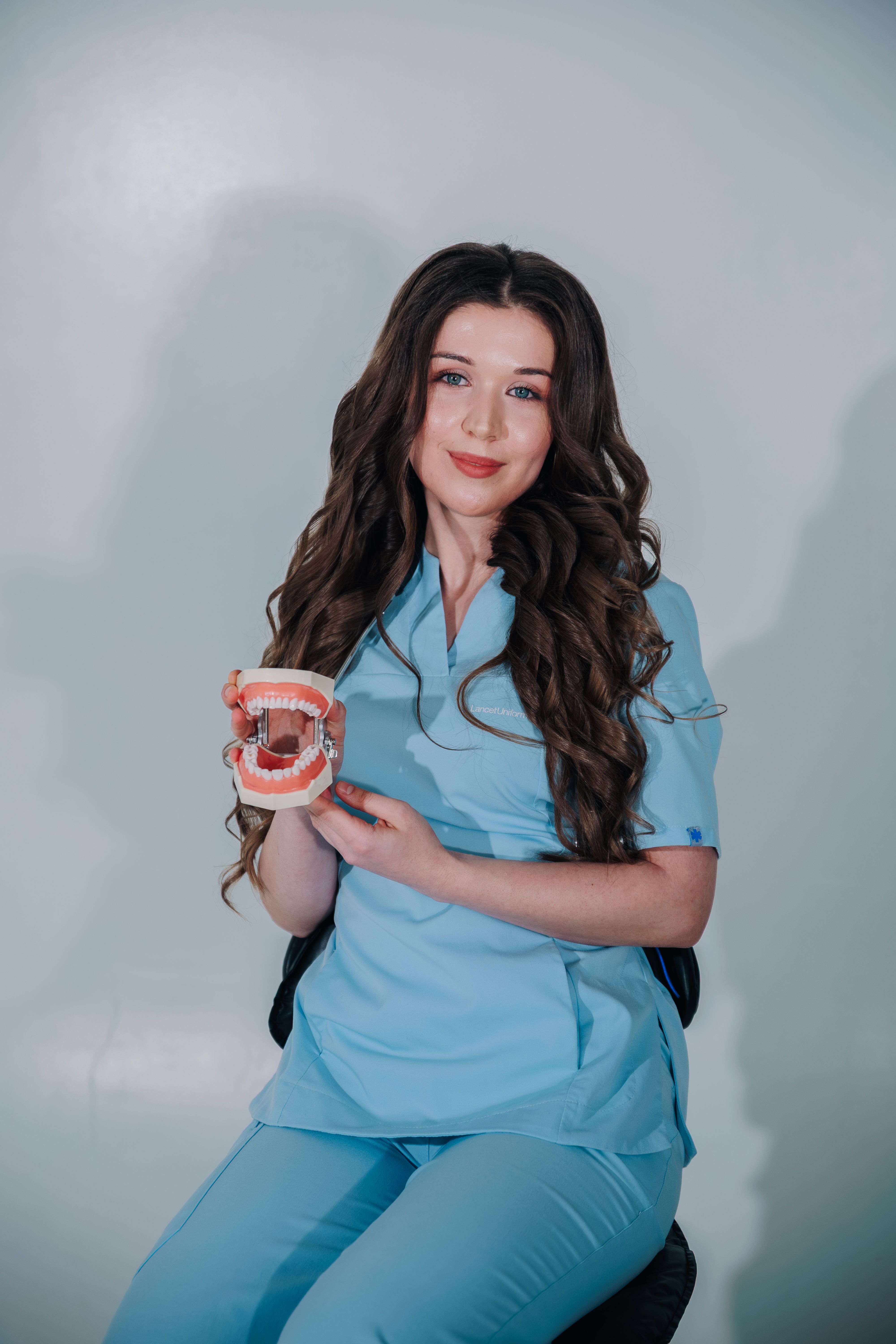 Female dentist in scrubs holding a dental model. Perfect for healthcare and dental care themes.