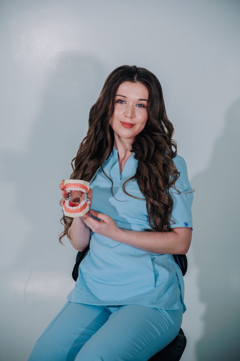 Dr. Anna Keller, a female dentist in light blue scrubs holding a tooth model