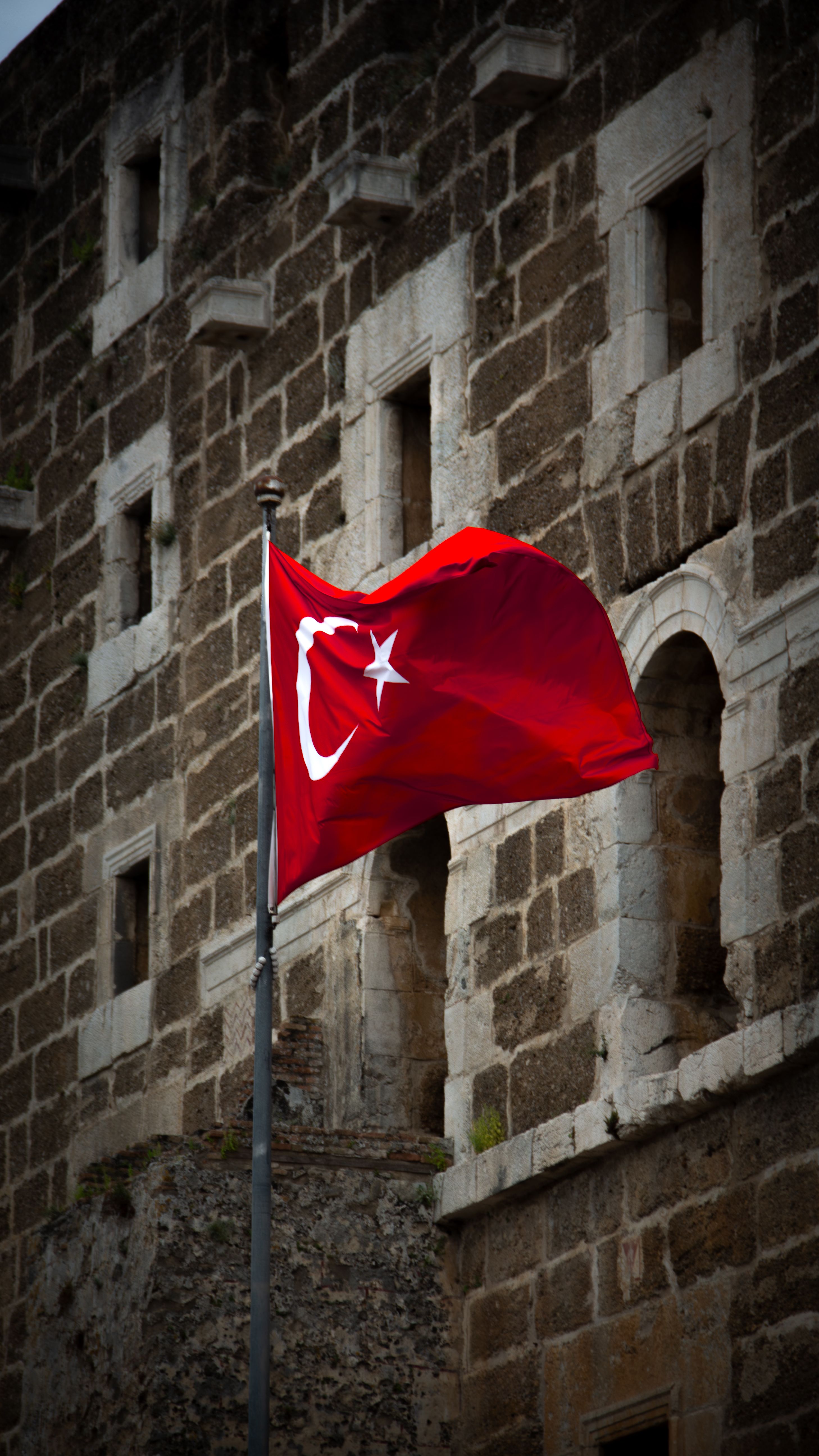 Majestic Turkish flag waving in front of a historic stone building in Antalya, Türkiye, symbolizing national pride.